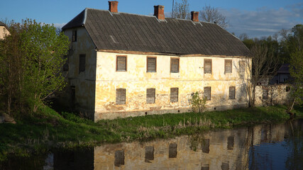 Fototapeta na wymiar An old, abandoned house with covered windows at the river. The loss of cultural heritage in Europe. The real estate market. Dobele town, Latvia in the spring of 2019.