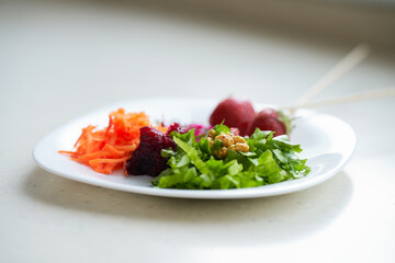 A white plate with vegetables, chard sprouts and garden strawberries strung on chopsticks. Selective focus.