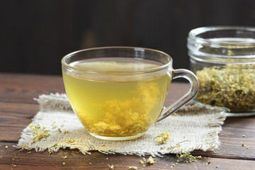 Meadowsweet floral herbal tea in glass cup with dried herb in a jar nearby on the wooden rustic table, closeup, copy space, natural medicine and healthy herbal tea concept