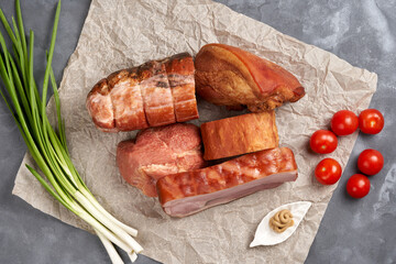 Variety of smoked pork with cherry tomatoes and green onions on parchment. View from above. Assorted semi-finished meat products.