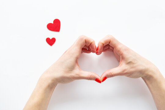 Female hands in the shape of a heart isolated on a white background, side view of small red hearts.