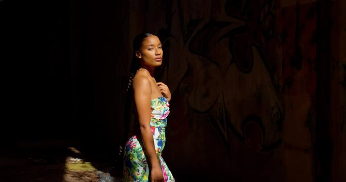 A sexy girl stands in the light and dark shadows of an abandoned warehouse
