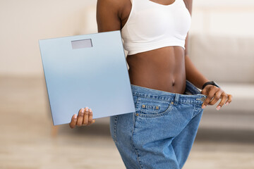 Slim Woman Holding Scales Wearing Large Jeans After Slimming Indoors