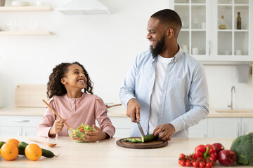 African american father and daughter cooking tasty salad