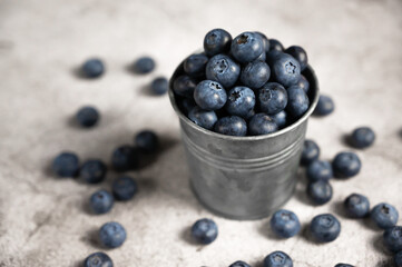 Fresh blueberries in a small metal bucket surrounded with some berries against concrete background. Top view. Rustic.