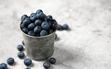 Fresh blueberries in a small metal bucket surrounded with some berries against concrete background. Top view. Rustic.