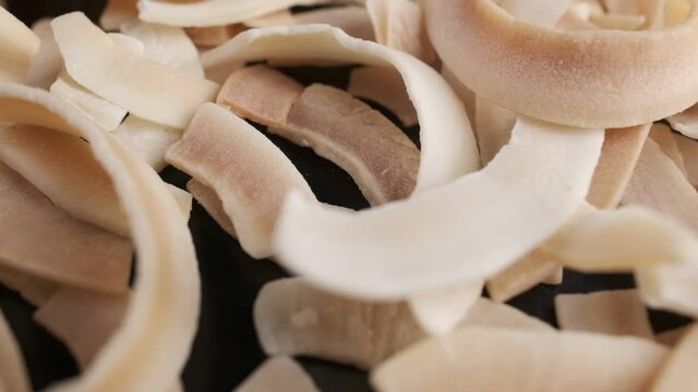 Coconut chips on a dark table close-up. Black background, slow motion.
