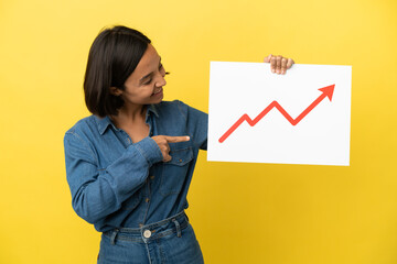 Young mixed race woman isolated on yellow background holding a sign with a growing statistics arrow symbol and  pointing it