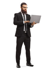 Full length portrait of a bearded man in a suit standing and using a laptop computer