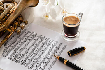 Black coffee cup on a music score with trumpet and flower
