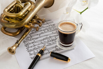 Black coffee cup on a music score with trumpet and flower
