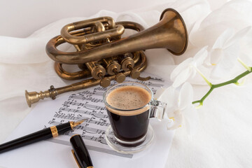 Black coffee cup on a music score with trumpet and flower

