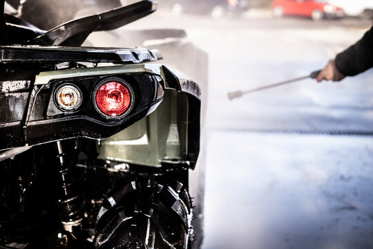 A Young Man Is Washing His Dirty ATV On The Car Wash.
