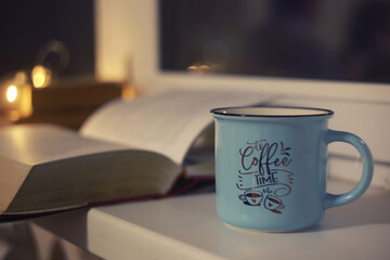 Closeup blue cup of coffee with vintage books on windowsill in early morning. Vintage light, blurred and bokeh background. Cosiness, warm and reading concept