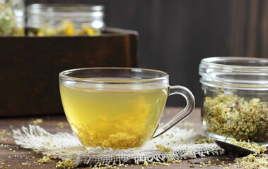 Meadowsweet floral herbal tea in glass cup on vintage books with dried herb in a jar nearby on the wooden rustic table, closeup, copy space, natural medicine and healthy herbal tea concept
