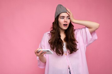 Photo of attractive crazy amazed surprised young woman wearing casual stylish clothes standing isolated over background with copy space holding and using mobile phone looking to the side