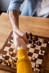 partial view of father and son shaking hands near chessboard, blurred background