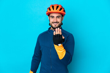 Young cyclist man isolated on blue background inviting to come with hand. Happy that you came