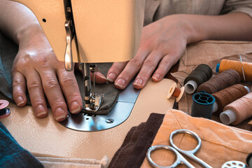 Women's hands sew on a sewing machine against the background of fabrics and threads. Horizontal orientation.