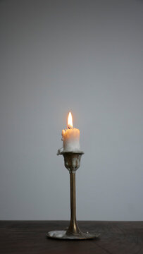 Porta velas de lat&oacute;n con vela de cera gastada sobre mesa de madera y pared blanca