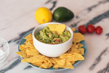 Guacamole and corn chips in a bowl, on a marble table