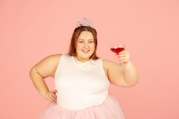 Cheers. Beautiful plump caucasian plus size model in fairy's outfit isolated on pink studio background. Concept of inclusion, human emotions, facial expression, sales, body positive. Copyspace for ad.