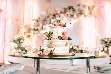 The wedding cake. White, two-tiered, decorated with flowers and gold. On a delicate pink background. Side view, top.