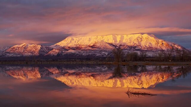 Snow capped mountain reflecting in water moving in slow motion at sunset as the mountains glows in Utah.
