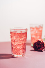 Red drink cocktail or lemonade with ice in a glass on pink background.