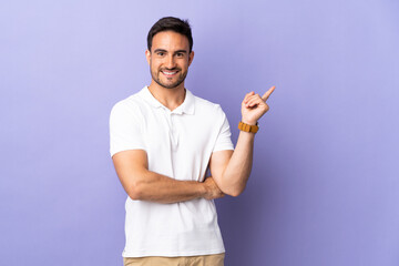 Young handsome man isolated on purple background happy and pointing up