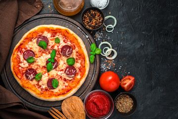 Pizza with salami, tomatoes and cheese on a black background. Top view with copy space.