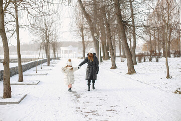 Family in knitted winter hats on family Christmas vacation. Woman and little girl in a park. People walks.