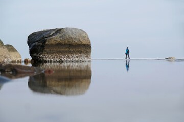 Silhouette of walking woman with poles on horizon of sea with very calm water. Oslonino, Baltic Sea, Poland