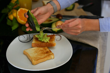 girl preparing toast with avocado and fruit on the kitchen table