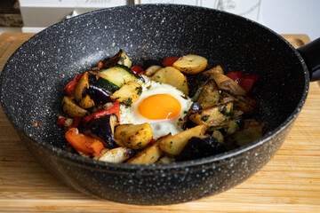 Serve one fried egg with baked vegetables, sausage. Round bright yellow yolk in the center.