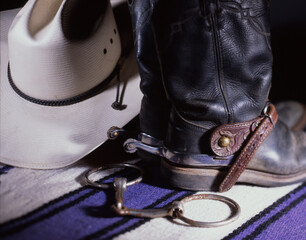 Close up of Black Western Boots with Rowel Spurs, Straw Western Hat and Snaffle Bit with a Purple Wood Pad in Studio Lighting