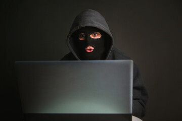 An angry hacker in a mask with a hood infiltrates data servers and infects their systems with...