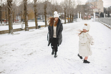 Family in knitted winter hats on family Christmas vacation. Woman and little girl in a park. People walks.