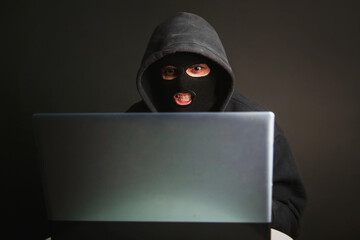 An angry hacker in a mask with a hood infiltrates data servers and infects their systems with...