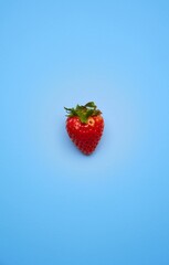 Fruit placed in the center on a plain blue background. Appetizing strawberry on a homogeneous light blue background.