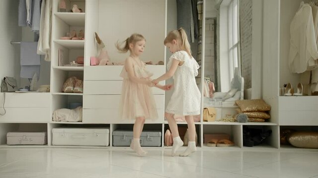 Dancing little girls enjoy new dress in clothing room on backdrop of wardrobe with clothes. Childhood, fashion and style