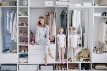 Female wardrobe. Stylish mother, cute twin daughters wearing comfortable home clothes posing in...