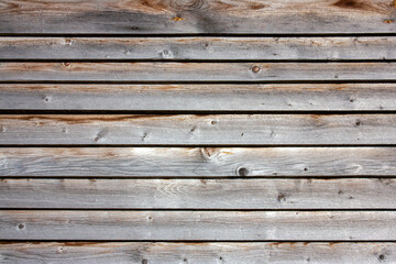 Facing the house with horizontal boards. Boards on the wall of the house close-up. The sun is shining on the old boards. Rough texture of real natural wood. Natural wood, side view.