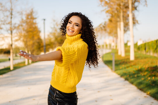 On the path of autumn park in a bright thick warm sweater whirling girl with dark curly hair and broadly white-toothed smiles. High quality photo