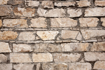 Fragment of a wall made of stones of different sizes. Close-up of a rough stone wall. Part of a stone wall on a sunny day.