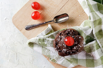 Chocolate cupcake with icing on napkin on wooden board and old spoon.