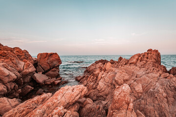 Fototapeta na wymiar Beautiful sunset seascape in Italy, Sardinia island. Red and pink rocks, wind erosion, geology stratification, air oxidation. Teal and orange lighting, endless horizon and soft pastel colored clouds.
