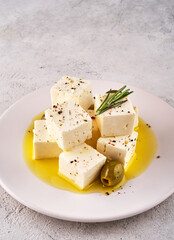 Feta cheese cubes with rosemary and olives in bowl on white background. Organic cheese concept.