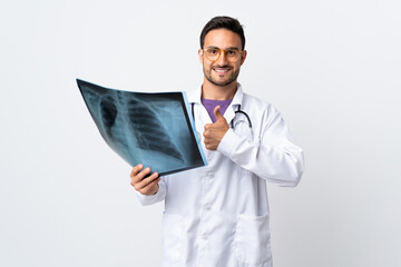 Young doctor man holding a radiography isolated on white background giving a thumbs up gesture