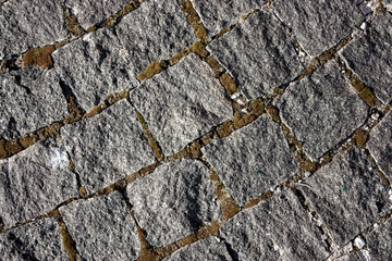 Obraz premium The sidewalk is paved with stones, top view. Grass and moss grow between the cobblestones on the pavement. Sharp edges of stones on a new pavement on a summer day.